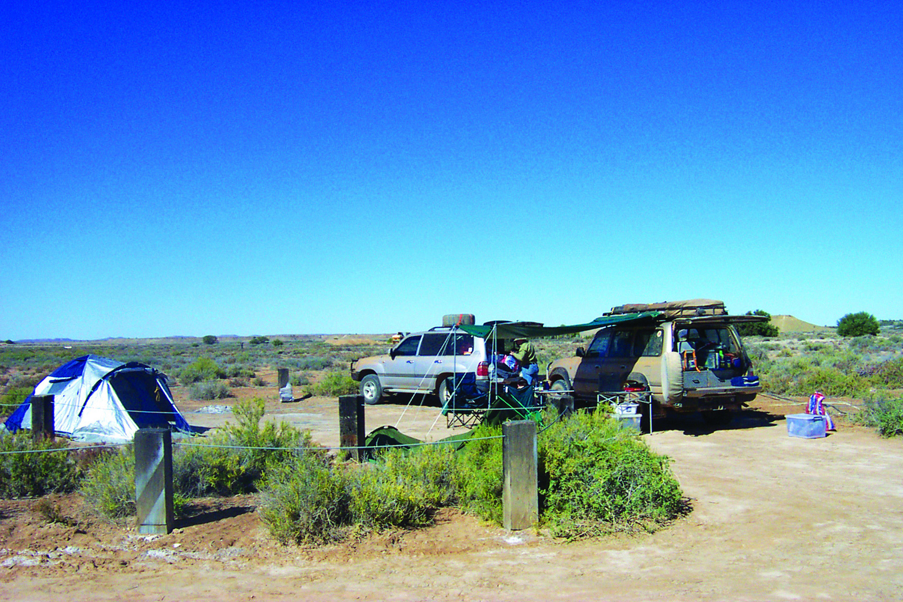 A setup in the outback of two cars, a tent and an awning on poles