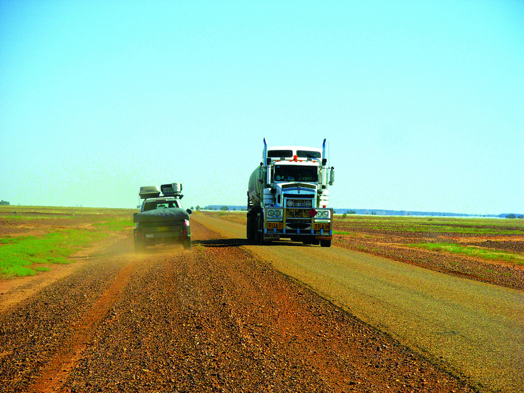 An open, barren road with a large, oncoming road train and a 4WD passing it