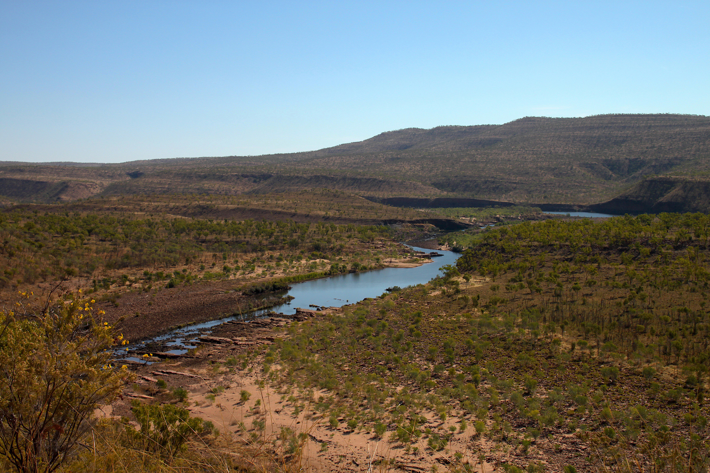 The landscape featuring bush scrub, water and mountains in the distance